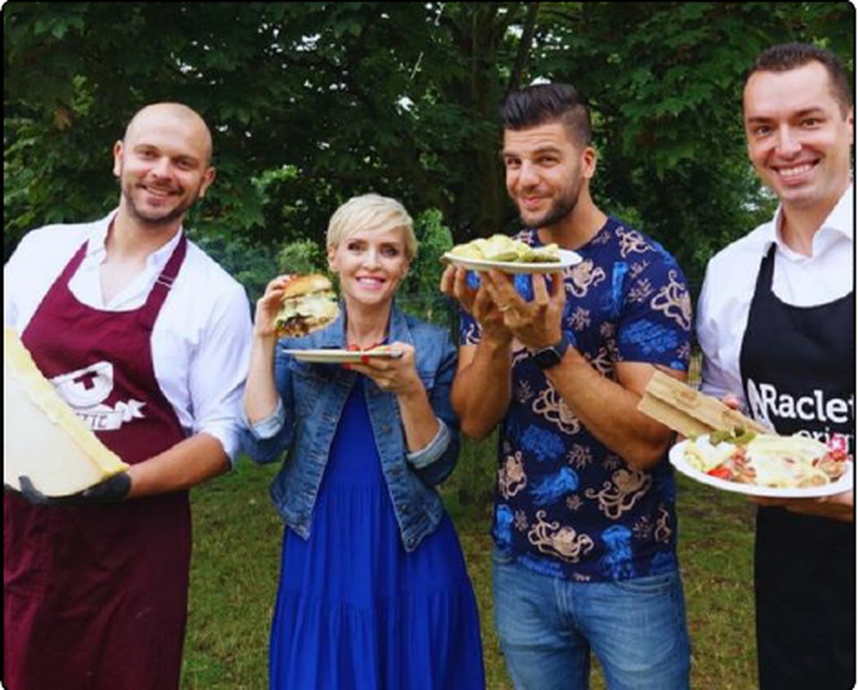Skupina s Milanem Kolářem a hosty s talíři raclette a burgery venku